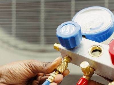 Close up of professional worker holding pressure indicators used for checking air conditioner freon tank in need of maintenance. Licensed serviceman using manifold gauges to check refrigerant levels